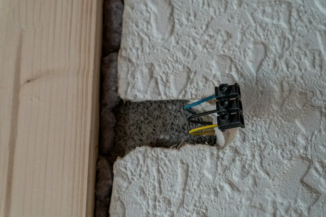Exposed electrical wires with a terminal block sticking out of an opening in a textured wall