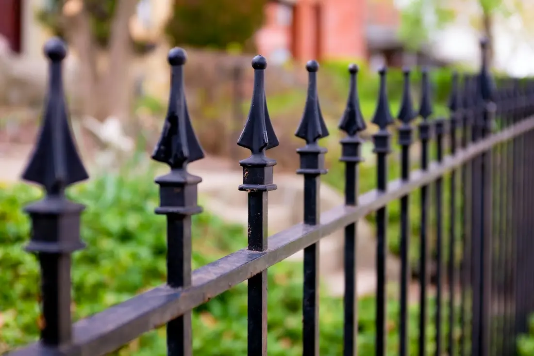 Black wrought iron fence with pointed spear-top pickets curving along a lawn with soft green shrubs behind it