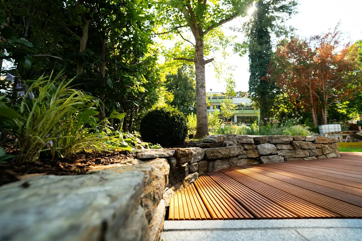 Finished backyard with a hardwood deck beside a dry stone retaining wall and planted beds
