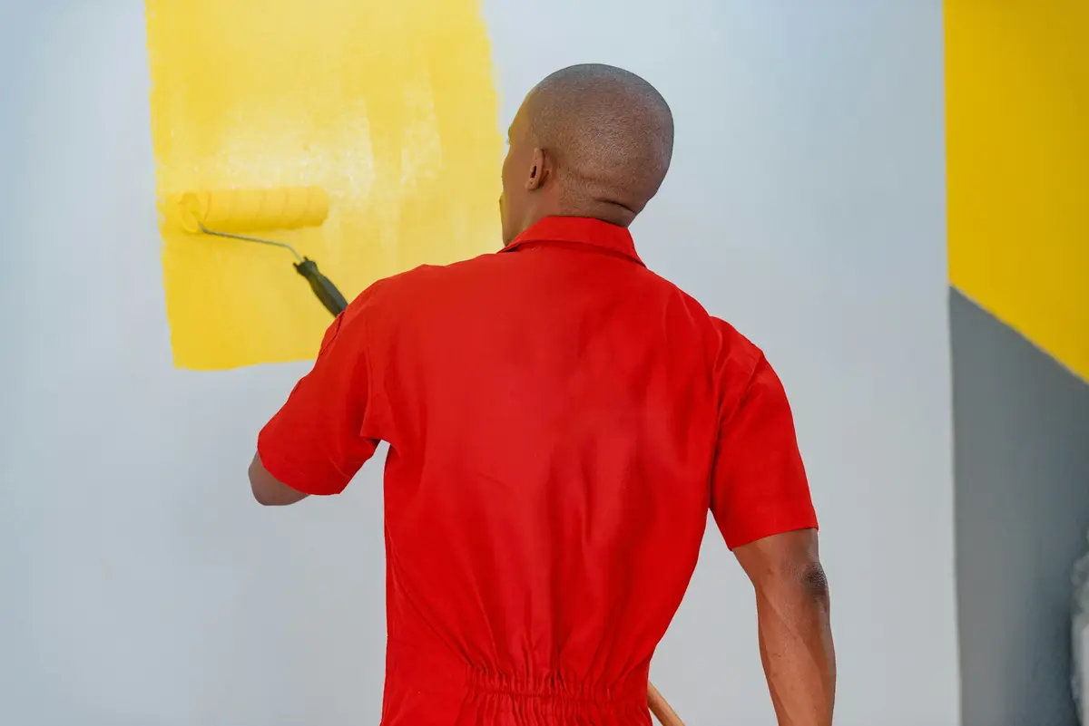 Painter in red coveralls rolling yellow paint onto an interior wall