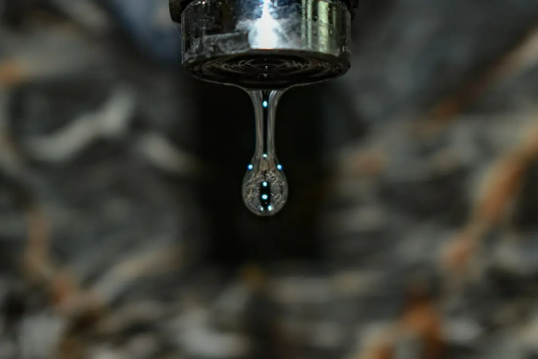 Water drop falling from a leaking chrome faucet, a common plumbing repair search
